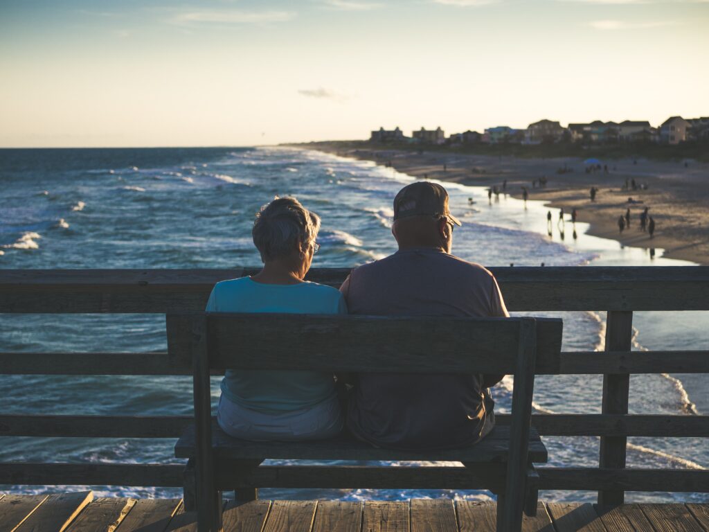 Photo of older couple in their 60s enjoying their retirement by looking out at the beach from a pier. For Money Guy article on Net Worth by Age